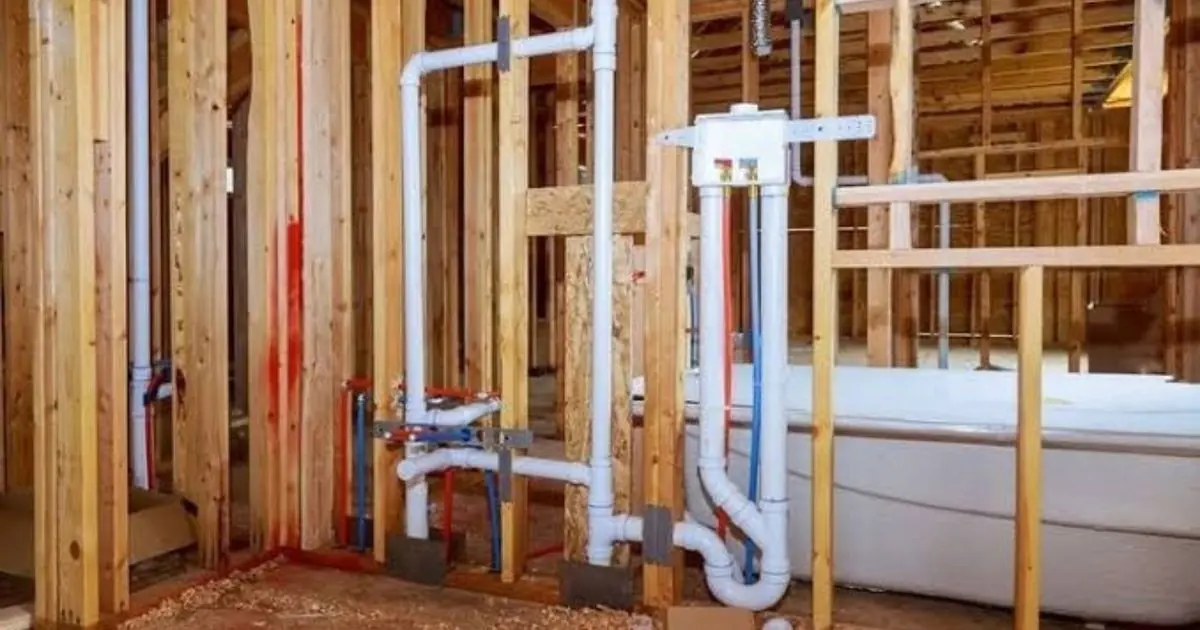 Open wall framing with white PVC drain and vent rough-in for a new bathroom