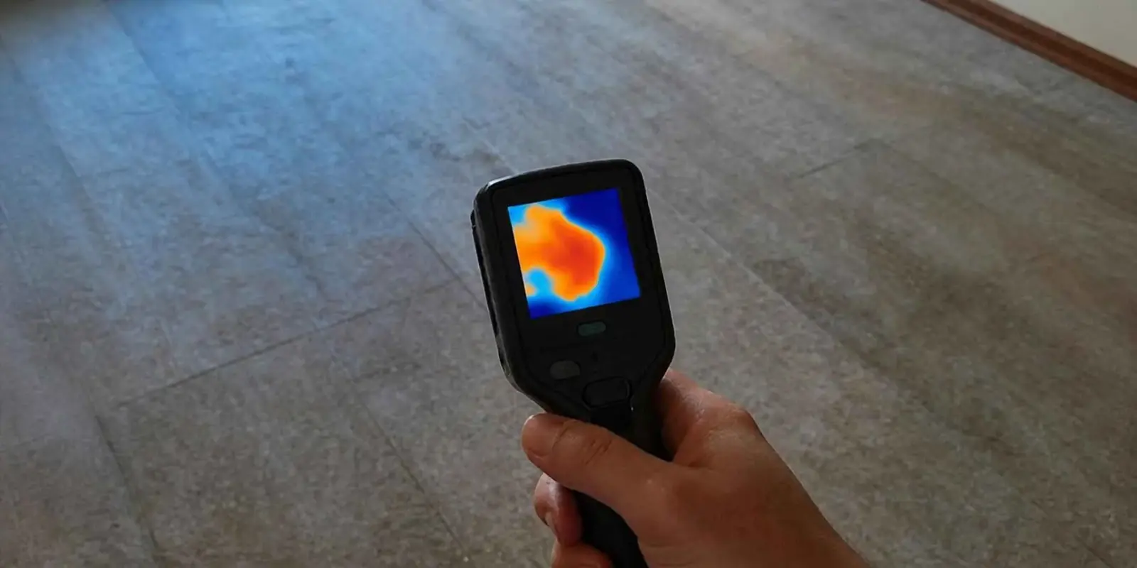 Handheld thermal camera pointed at a floor to look for a heat pattern from a leak